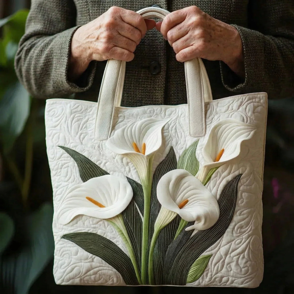 White quilted tote bag with lily floral applique, shown with hands gripping handles