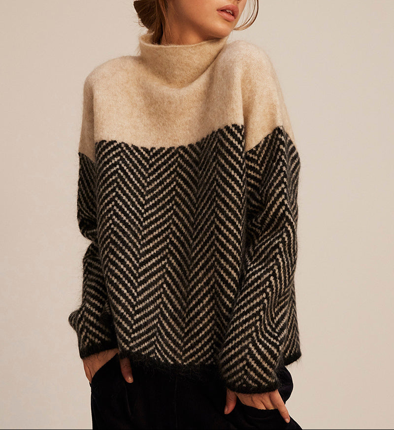 Beige knit turtleneck pullover with black chevron front panel and long sleeves, ribbed collar.