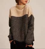 Beige knit turtleneck pullover with black chevron front panel and long sleeves, ribbed collar.